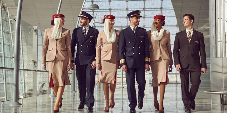 Mehrere uniformierte Emirates Mitarbeitende gehen nebeneinander durch eine lichtdurchflutete Flughafenhalle mit Glasarchitektur