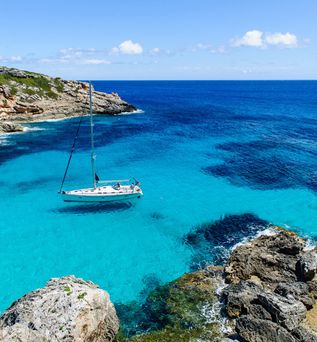 Segelboot auf klarem türkisblauem Wasser in einer felsigen Bucht unter blauem Himmel