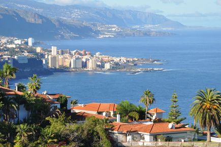 Blick auf eine Küstenstadt mit mehreren Gebäuden, Palmen und dem Meer im Hintergrund
