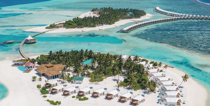 Luftaufnahme einer tropischen Insel auf den Malediven mit weißen Sandstränden, Palmen und über dem Wasser gebauten Bungalows