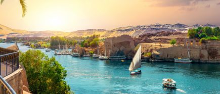 Nil mit Segelbooten und Motorbooten vor antiken Ruinen und felsiger Landschaft bei Sonnenuntergang