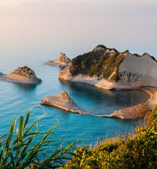 Blick auf die felsige Küste und das blaue Meer der Insel Korfu in Griechenland, mit grüner Vegetation im Vordergrund