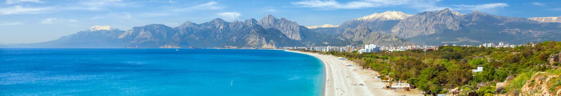 Panoramablick auf den Konyaalti-Strand in Antalya, Türkei, mit türkisblauem Meer, breitem Sandstrand und imposanten Taurusgebirgen im Hintergrund