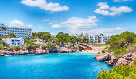 Blaue Badebucht Cala Esmeralda in Cala d’Or auf Mallorca, umgeben von Felsen, Pinien und weißen Hotels