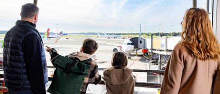 Familie am Gate im Flughafen Hamburg beobachtet startende und parkende Flugzeuge auf dem Rollfeld