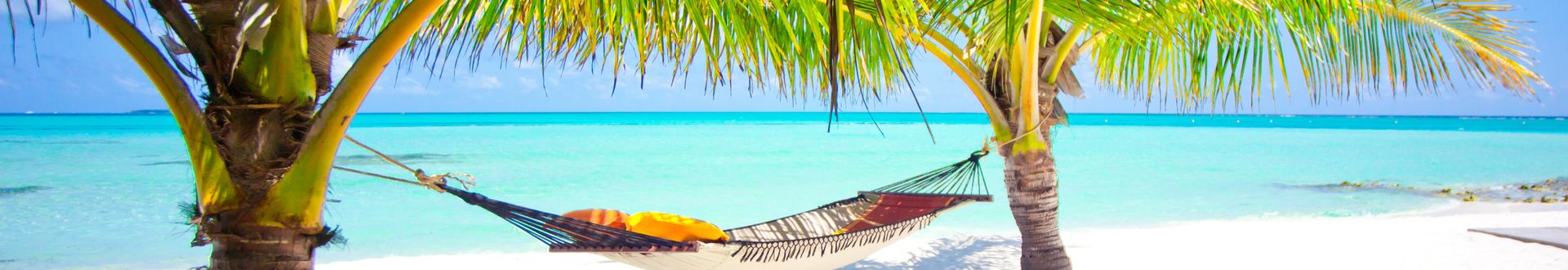 Hängematte zwischen Palmen am weißen Sandstrand mit türkisfarbenem Meer im Hintergrund