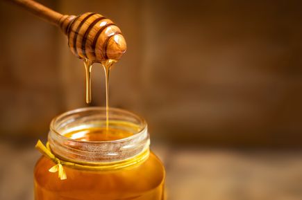 Honig, der von einem Holzlöffel in ein Glas mit gelbem Band tropft.