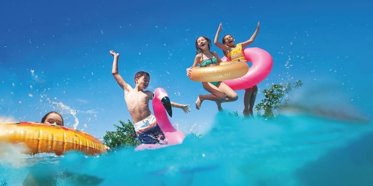 Kinder springen mit Schwimmreifen in einen Pool und haben Spaß im Wasser unter blauem Himmel