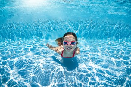 Kind mit Schwimmbrille taucht unter Wasser in einem klaren Swimmingpool