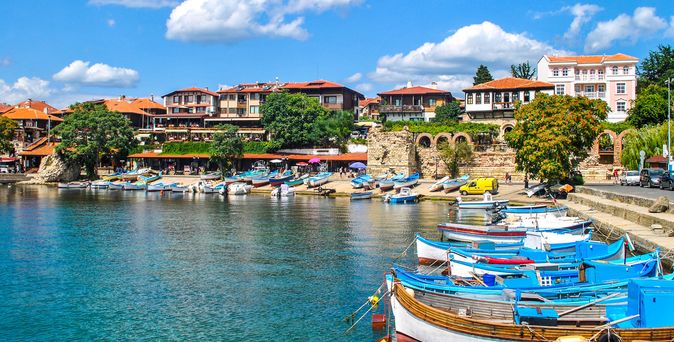 Kleiner Hafen mit bunten Booten und traditionellen Häusern am Wasser in Bulgarien unter blauem Himmel