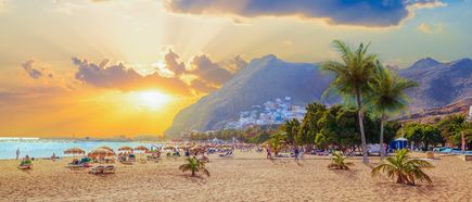 Strand Playa de Las Teresitas auf Teneriffa mit goldenem Sand, Palmen, Sonnenschirmen und Blick auf die umliegenden Berge bei Sonnenuntergang