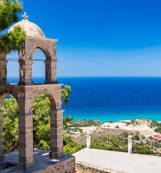 Steinerner Glockenturm mit Kreuz auf einer Anhöhe, Blick auf das blaue Meer und Küstenlandschaft bei Kos