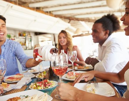 Menschen sitzen an einem gedeckten Tisch und genießen gemeinsam eine Mahlzeit mit verschiedenen Speisen und Getränken