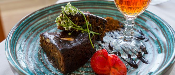 Traditioneller Bolo de Mel aus Madeira auf einem Teller mit Erdbeeren, Schokoladensauce und einem Glas Likör als regionale Spezialität der Insel