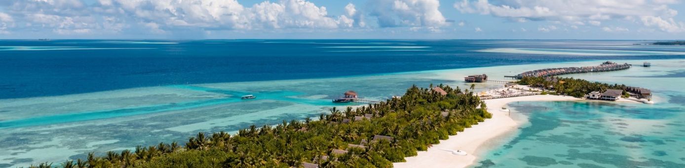 Luftaufnahme des Hotels OZEN Life Maadhoo auf den Malediven mit weißem Sandstrand, Palmen und türkisfarbenem Meer