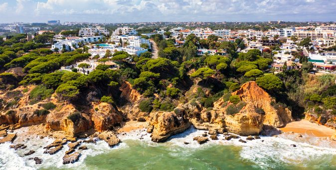 Küstenlinie von Albufeira mit Felsen, Pinien und weißen Gebäuden unter blauem Himmel