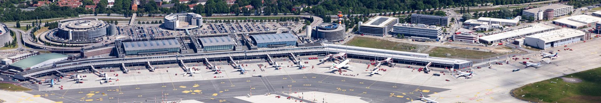 Luftaufnahme des Flughafens Hamburg mit Terminals, Vorfeld und geparkten Passagierflugzeugen sowie Parkhäusern und Zufahrtsstraßen rund um den Airport
