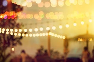 Warme, bunte Bokeh-Lichter über einer sommerlichen Outdoor‑Location mit Lichterketten und weichem Sonnenuntergangslicht, das eine entspannte Strand‑Atmosphäre erzeugt