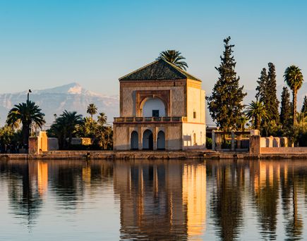 Historisches Gebäude am Ufer eines ruhigen Sees mit Palmen und Bergen im Hintergrund bei klarem Himmel