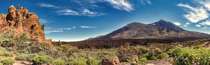 Panoramablick auf den Teide, umgeben von vulkanischem Gestein und grünen Pflanzen im Vordergrund.