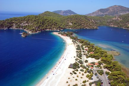 Weitläufige Lagune bei Ölüdeniz mit ruhigem, tiefblauem Wasser, geschwungenem Sandstrand und grünen Hügeln im Hintergrund