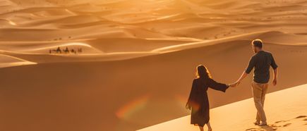 Paar hält sich an den Händen und spaziert bei Sonnenuntergang durch die Wüste