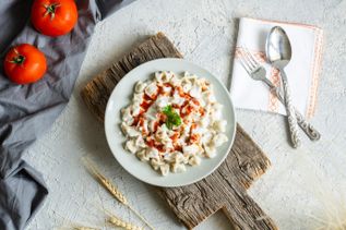 Türkische Manti mit Joghurtsoße und Paprikabutter auf Teller, Draufsicht mit Besteck und Tomaten