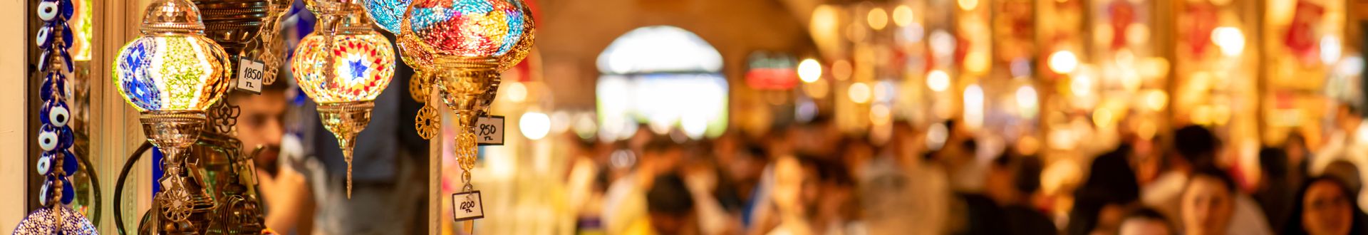 Panoramablick im Gewürzbasar Istanbul: leuchtende orientalische Glaslampen im Vordergrund, dahinter eine dicht gedrängte Menschenmenge in der Markthalle