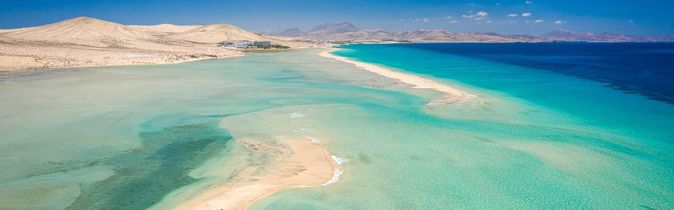 Landschaft der Kanarischen Inseln mit türkisfarbenem Meer, Sandbänken und Bergen im Hintergrund