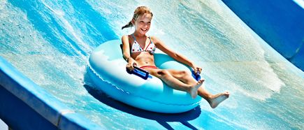 Mädchen rutscht lachend auf einem blauen Schwimmreifen eine große Wasserrutsche hinunter