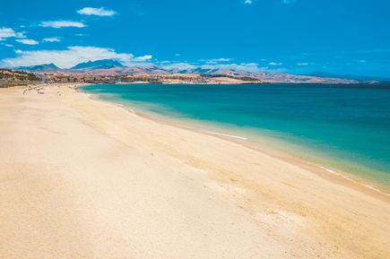 Breiter Sandstrand mit wenigen Menschen und klarem, ruhigem Meer unter blauem Himmel