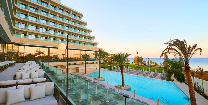 Außenansicht des Sunrise Emerald mit modernem Hotelgebäude, großzügigem Poolbereich, Palmen, Liegen und Blick auf das Meer bei Sonnenuntergang
