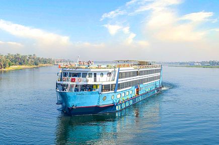 Das Flusskreuzfahrtschiff MS Magic I fährt über den Nil, umgeben von ruhigem Wasser, grüner Uferlandschaft und hellem Himmel mit vereinzelten Wolken