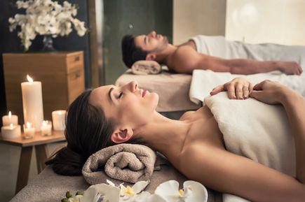 Zwei nebeneinanderstehende Massageliegen in einem modernen Wellnessbereich, mit weißen Handtüchern und beruhigender Beleuchtung