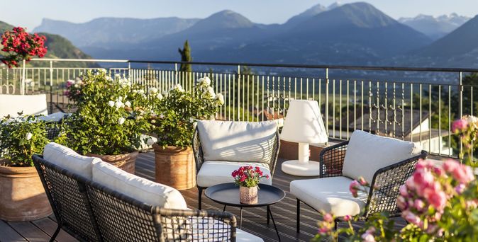 Terrasse mit Sitzgruppe aus Korbmöbeln, Tisch mit Blumen und Blick auf Berge im Hintergrund