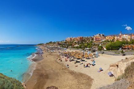Breiter Strand mit Hotelgebäuden im Hintergrund, Sonnenschirmen unter blauem Himmel 