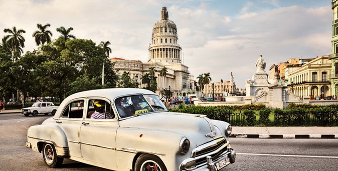 Oldtimer fährt vor dem Kapitol von Havanna, Kuba, mit Palmen und historischen Gebäuden im Hintergrund