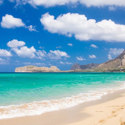 Sandstrand mit türkisfarbenem Meer, bewölktem Himmel und Bergen im Hintergrund an der Küste von Falassarna auf Kreta.