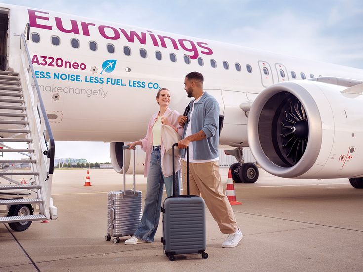 Zwei Reisende mit Rollkoffern auf dem Flughafenvorfeld vor einem Eurowings Airbus A320neo