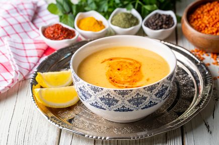 Cremige türkische Linsensuppe in gemusterter Schale, mit Paprikaöl verfeinert und Zitronenspalten daneben