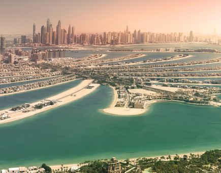 Luftaufnahme von Dubai mit künstlichen Inseln in Form von Palmen und einer Skyline mit Wolkenkratzern im Hintergrund