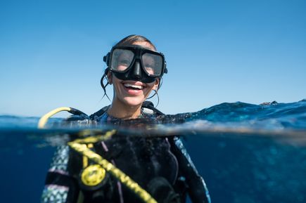 Taucherin mit Tauchmaske und Atemregler im Wasser, halb unter Wasser fotografiert