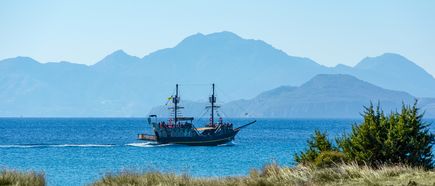 Segelschiff mit zwei Masten auf ruhigem Meer vor bergiger Küstenlandschaft