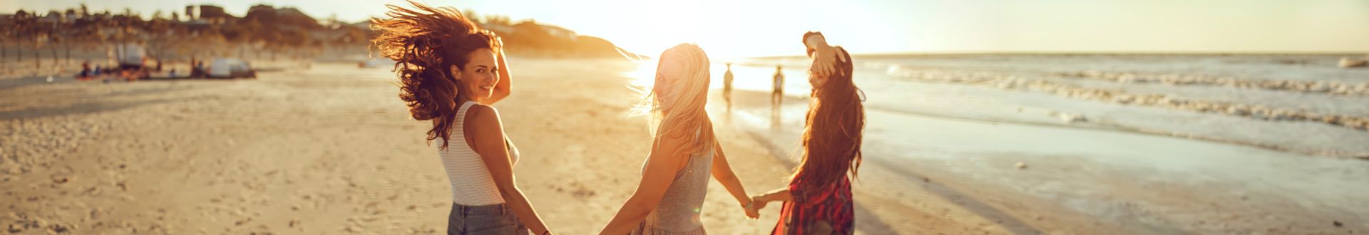 Drei Frauen laufen am Strand bei Sonnenuntergang händchenhaltend in Richtung Wasser