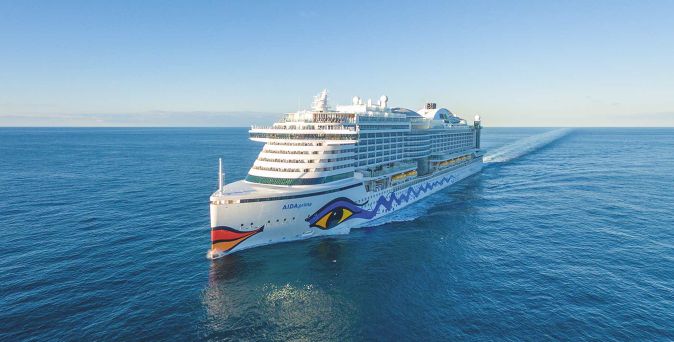 Das moderne Kreuzfahrtschiff AIDAprima fährt durch ruhiges, blaues Meer und hinterlässt eine lange weiße Bugwelle
