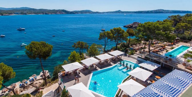 Küstenhotel mit Pool und weißen Sonnenschirmen, umgeben von Pinien und mit weiter Aussicht auf das Meer.
