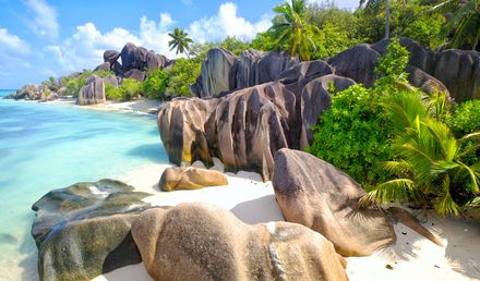 Strand Anse Source d’Argent auf der Insel La Digue auf den Seychellen mit hellem Sand, türkisfarbenem Wasser, imposanten Granitfelsen und üppigen Palmen unter blauem Himmel