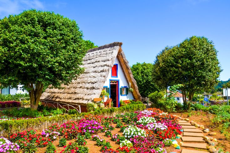 Traditionelles strohgedecktes Haus in Santana auf Madeira, umgeben von Blumenbeeten, Bäumen und gepflegten Gartenanlagen